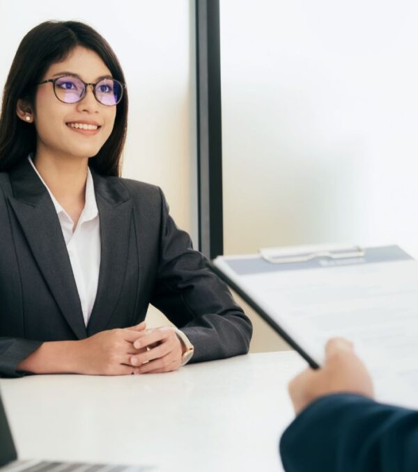 Woman sitting with good posture and smiling at job interview with interviewer holding her resume