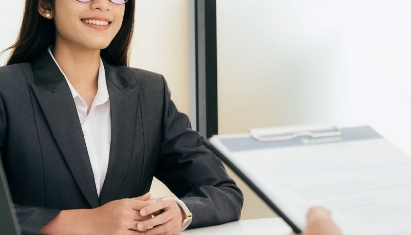 Woman sitting with good posture and smiling at job interview with interviewer holding her resume